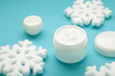 Soğuk koruma kremi konsepti. Mavi zemin üzerinde kar taneleri olan kavanoz kozmetikleri.