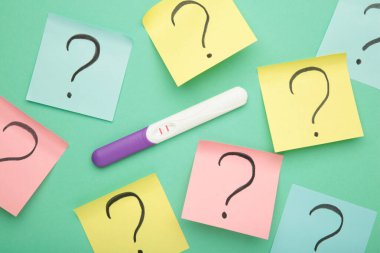 Tek şeritli hamilelik testi ve yepyeni bir arkaplanda soru işaretleri. Pozitif sonuç.