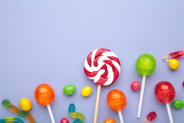 Different types of candies on purple background, copy space. Colorful birthday party background.