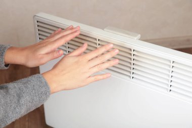 Genç bir kadın ve küçük bir kız modern elektrikli ısıtıcının yanında ellerini ısıtıyorlar. Üst görünüm