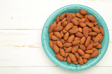 Taze, sağlıklı badem, beyaz ahşap arka planda mavi tabakta fındık. Üst