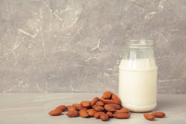 Cam şişede taze badem sütü ve gri arka planda badem. Sağlıklı vejetaryen bitki temelli alternatif süt değiştirici.