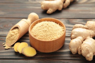 Kahverengi ahşap zemin üzerinde taze zencefil kökü olan zencefil tozu..