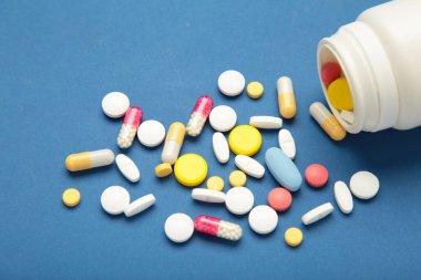 Çeşitli ilaç hapları, haplar, kapsüller ve mavi arka planda bir şişe. Üst görünüm