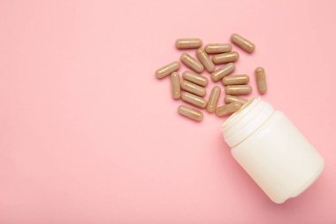 Bej ilaç hapları ve pembe arka planda bir şişe. Üst görünüm