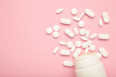 Çeşitli ilaç hapları ve pembe arka planda bir şişe. Üst görünüm