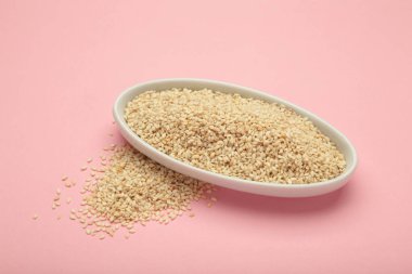 Pembe arka planda beyaz kasede çiğ susam tohumları. Üst görünüm.