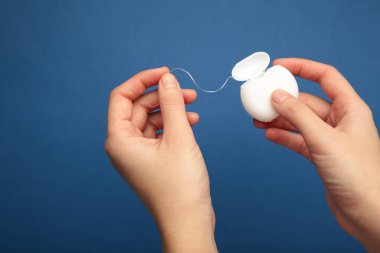 Mavi arka planda diş ipi tutan kadın eller. Diş sağlığı ve ağız sağlığı konsepti.