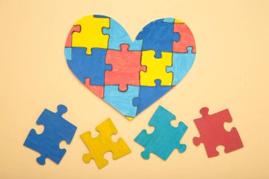 Bej arka planda renkli bir yapboz kalbi. Dünya Otizm Farkındalık Günü 'nün sembolü olarak çok renkli kalp