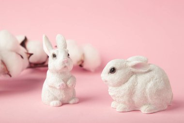 Pembe arka planda pamuk çiçekli beyaz seramik tavşanlar. Üst görünüm