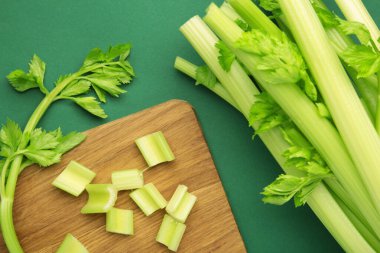 Yeşil arka planda kesme tahtasındaki taze yeşil kesim kereviz. Üst görünüm