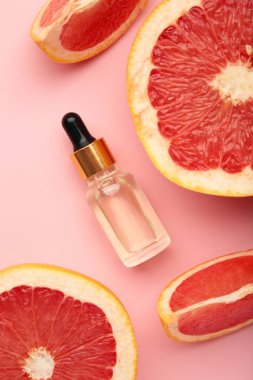 Bir şişe gerekli yağ ve pembe arka planda taze greyfurtlar. Üst görünüm
