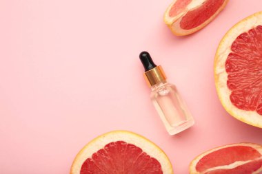 Bir şişe gerekli yağ ve pembe arka planda taze greyfurtlar. Üst görünüm