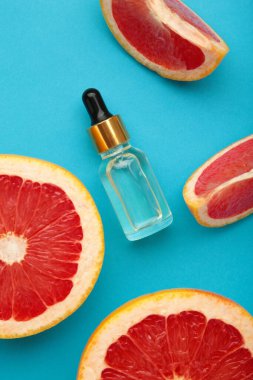 Bir şişe gerekli yağ ve mavi arka planda taze greyfurtlar. Üst görünüm