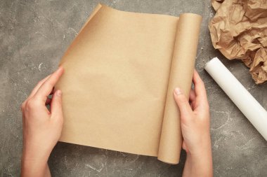 Gri beton arka planda bir rulo kağıt olan kadın eller. Üst görünüm