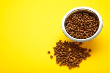 Sarı arka planda gümüş bir kasede kedi ya da köpek maması. Üst görünüm