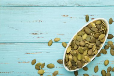 Mavi ahşap arka planda beyaz kasede kabak tohumları