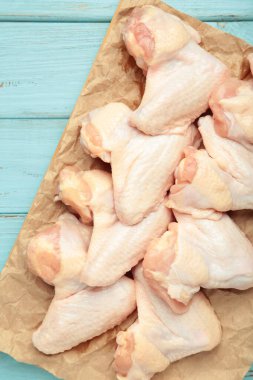 Mavi ahşap arka planda kesilmiş çiğ tavuk kanatları. Dikey fotoğraf. Üst görünüm