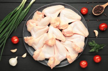 Siyah ahşap arka planda, koyu tabakta pişirmek için malzemeli çiğ tavuk kanadı.