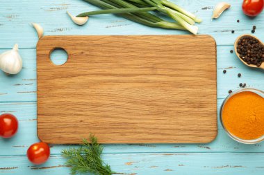 Kesme tahtası, yeşil soğan, sarımsak, baharatlar ve domatesler mavi ahşap arka planda. Yemek pişirme konsepti. Üst görünüm