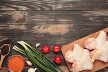 Çiğ tavuk kanadı, ahşap kesim tahtasında pişirmek için malzemelerle kahverengi ahşap arka plan, üst manzara.