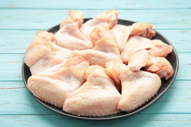 Mavi ahşap arka planda koyu tabakta çiğ tavuk kanadı. Üst görünüm