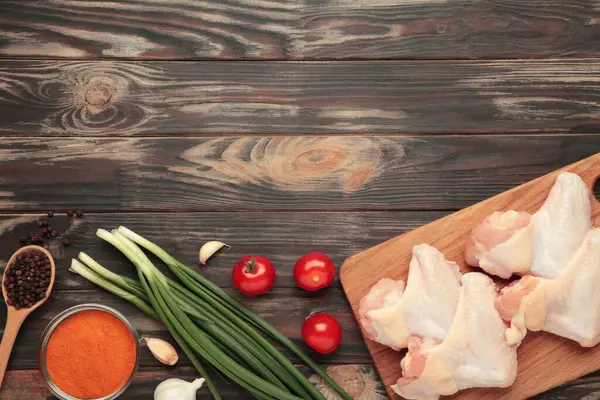 Çiğ tavuk kanadı, ahşap kesim tahtasında pişirmek için malzemelerle kahverengi ahşap arka plan, üst manzara.