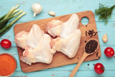 Çiğ tavuk kanadı, ahşap kesim tahtası ve ahşap arka planda yemek pişirmek için gerekli malzemeler.