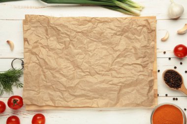 Beyaz ahşap zemin üzerinde yeşil soğanlı, sarımsaklı, baharatlı ve domatesli fırın kağıdı. Yemek pişirme konsepti. Üst görünüm