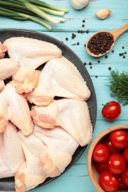 Mavi ahşap arka planda, koyu tabakta pişirmek için malzemeli çiğ tavuk kanadı.