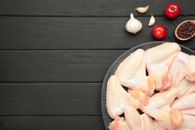 Siyah ahşap arka planda, koyu tabakta pişirmek için malzemeli çiğ tavuk kanadı.