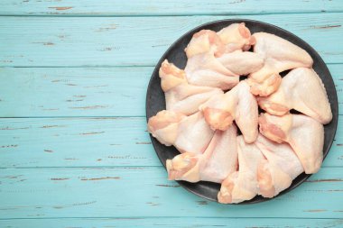 Mavi ahşap arka planda koyu tabakta çiğ tavuk kanadı. Üst görünüm