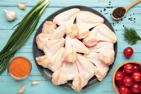 Mavi ahşap arka planda, koyu tabakta pişirmek için malzemeli çiğ tavuk kanadı.