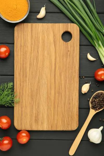 Kesme tahtası, yeşil soğan, sarımsak, baharatlar ve domatesler siyah ahşap arka planda. Yemek pişirme konsepti. Üst görünüm