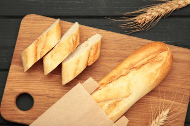 Ekmek bir bütün ve siyah arka planda kesme tahtasıyla parçalara ayrılmış. Metin için boşluk