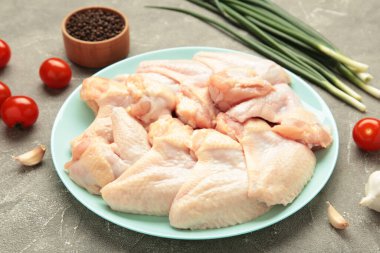 Çiğ tavuk kanadı. Gri arka planda, koyu tabakta pişirmek için malzemeler var.