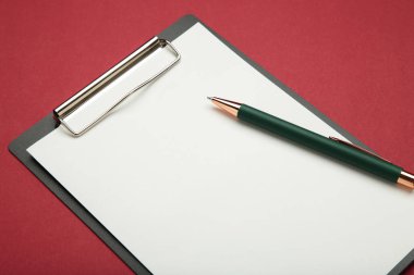 Kırmızı zemin üzerinde boş kağıt ve kalem olan siyah tablet. Üst görünüm