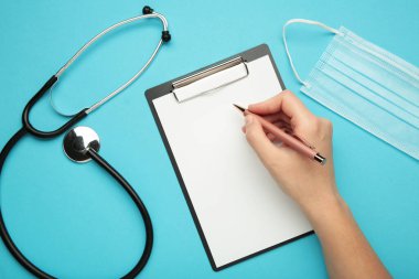 Bir kadın eli, modern steteskoplu bir kalem ve siyah pano tutuyor. Mavi arka planda mesajlar için yer var.
