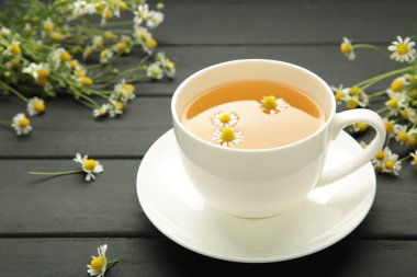 Beyaz fincanda romatik bitki çayı ve siyah fonda papatya çayı. Üst görünüm