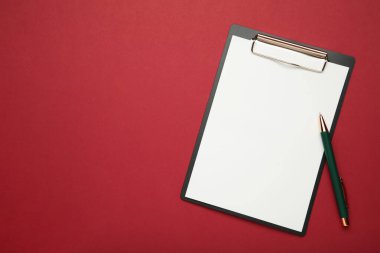 Kırmızı zemin üzerinde boş kağıt ve kalem olan siyah tablet. Üst görünüm