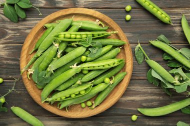 Tahta kasede taze yeşil bezelyeler ve kahverengi ahşap arka planda yapraklar. Üst görünüm