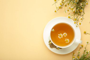 Beyaz fincanda Aromatik bitki çayı ve bej arka planda papatya çayı. Üst görünüm