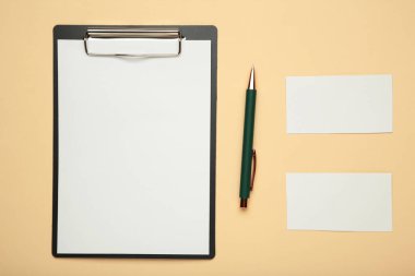 Boş kağıt maketli pano ve bej arka planda kırtasiye malzemesi.