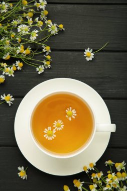 Beyaz fincanda romatik bitki çayı ve siyah ahşap arka planda papatya çayı. Üst görünüm