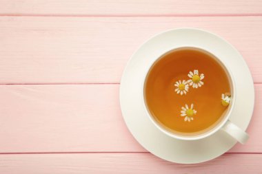 Beyaz fincanda aromatik bitki çayı ve pembe arka planda papatya çayı. Üst görünüm