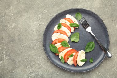 Çeri domatesli İtalyan Caprese salatası, mozzarella, gri arka planda koyu tabakta fesleğen..