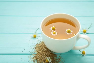 Beyaz fincanda romatik bitki çayı ve mavi arka planda papatya çayı. Üst görünüm