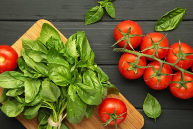 Siyah arka planda kiraz domatesleri ve yeşil fesleğen. Üst görünüm