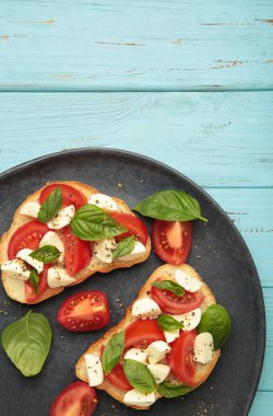 Mozarella peynirli lezzetli sandviç, domates ve lacivert arka planda koyu tabakta fesleğen. Caprese. Dikey fotoğraf