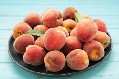 Tatlı şeftali ve yapraklar koyu tabakta mavi ahşap arka planda. Üst görünüm